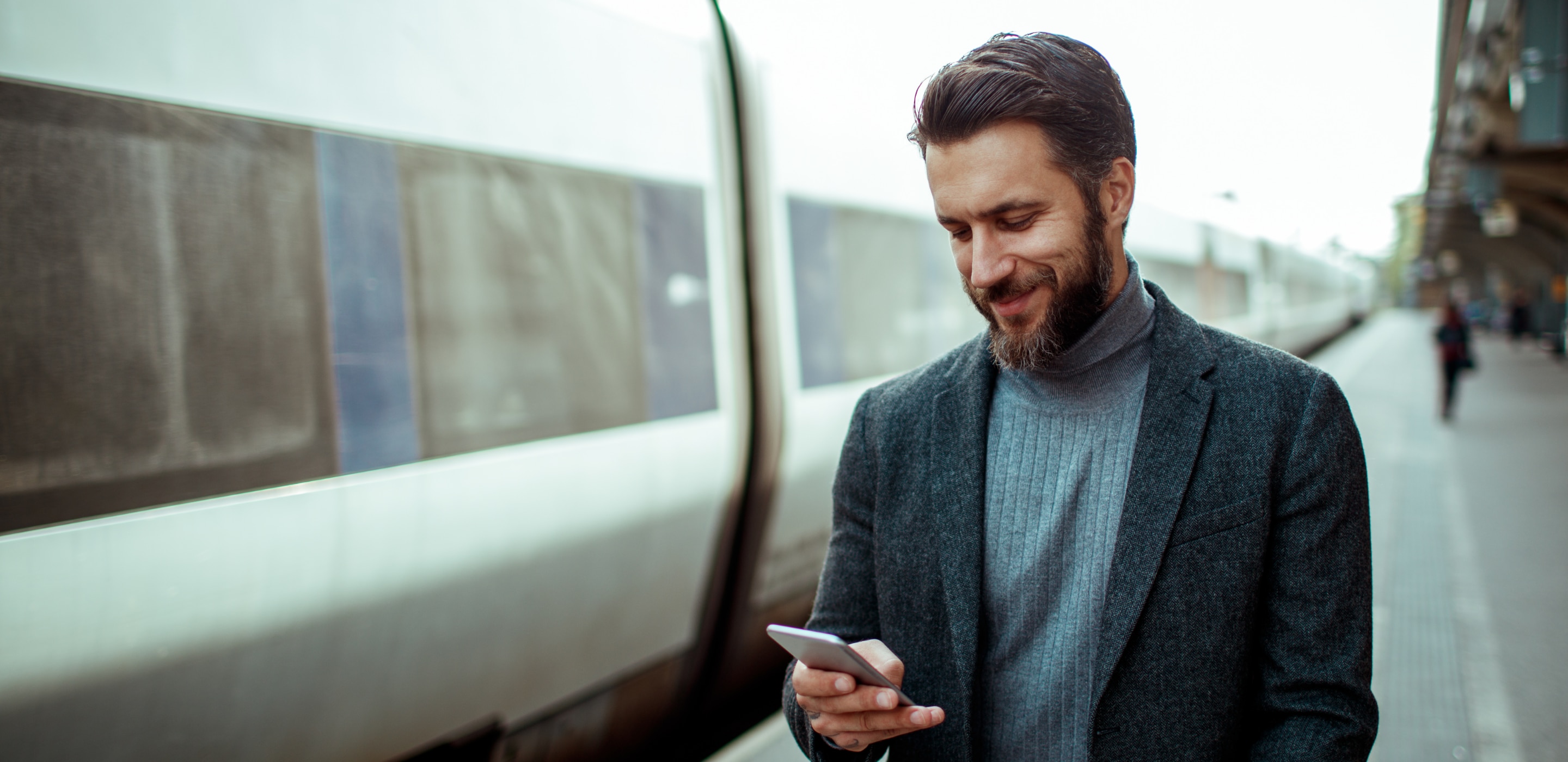 A man looking at a cellphone standing next to a train