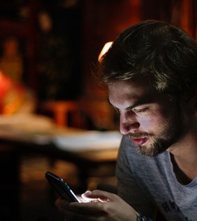 A man holding his phone in a room with side lamp on