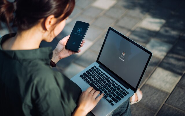 A woman holding a cellphone and typing on a laptop