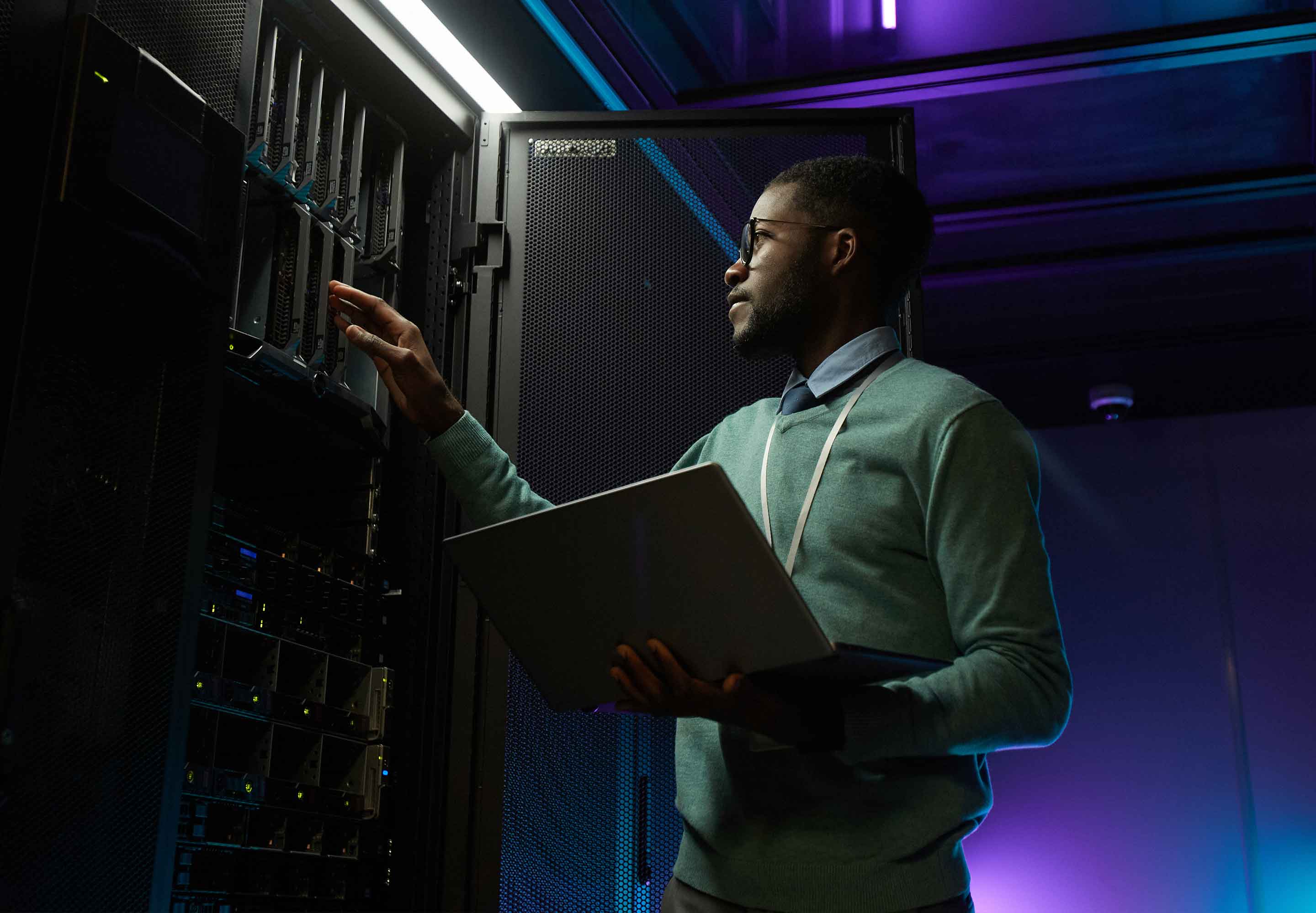 A man in a server room holding a laptop