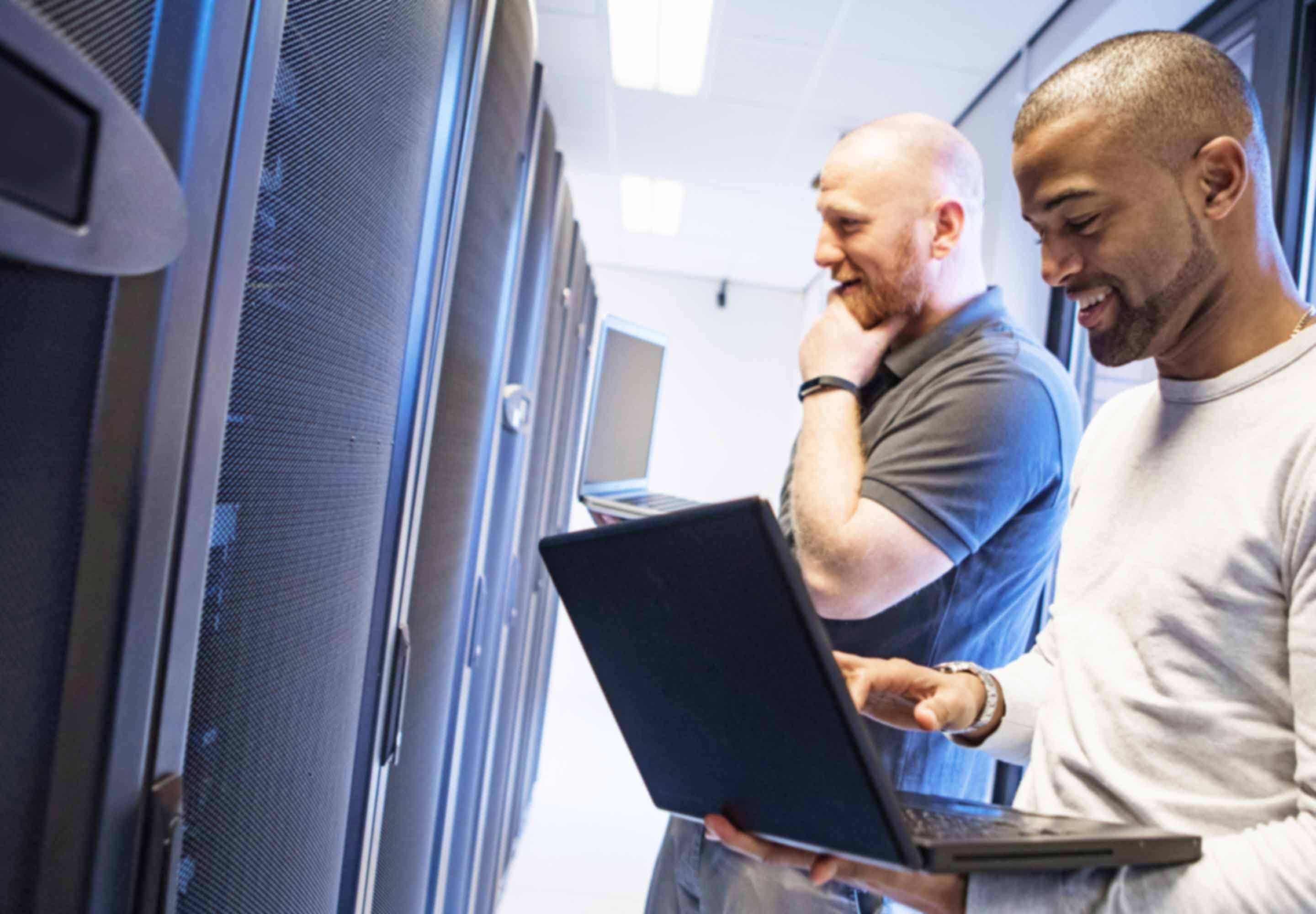 Two man in a server room one with laptop in his arms