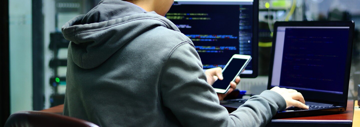 A person sitting in front of a laptop while on his phone