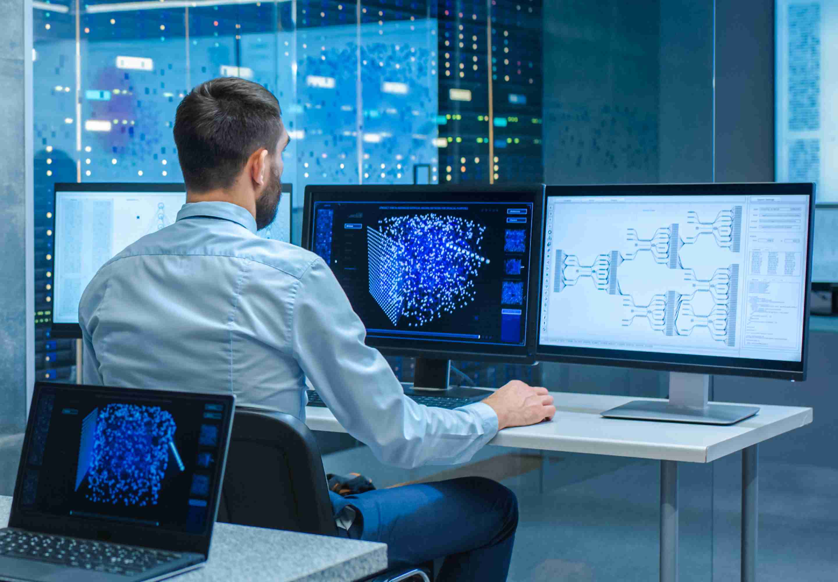 A man sitting and looking at three monitor screen