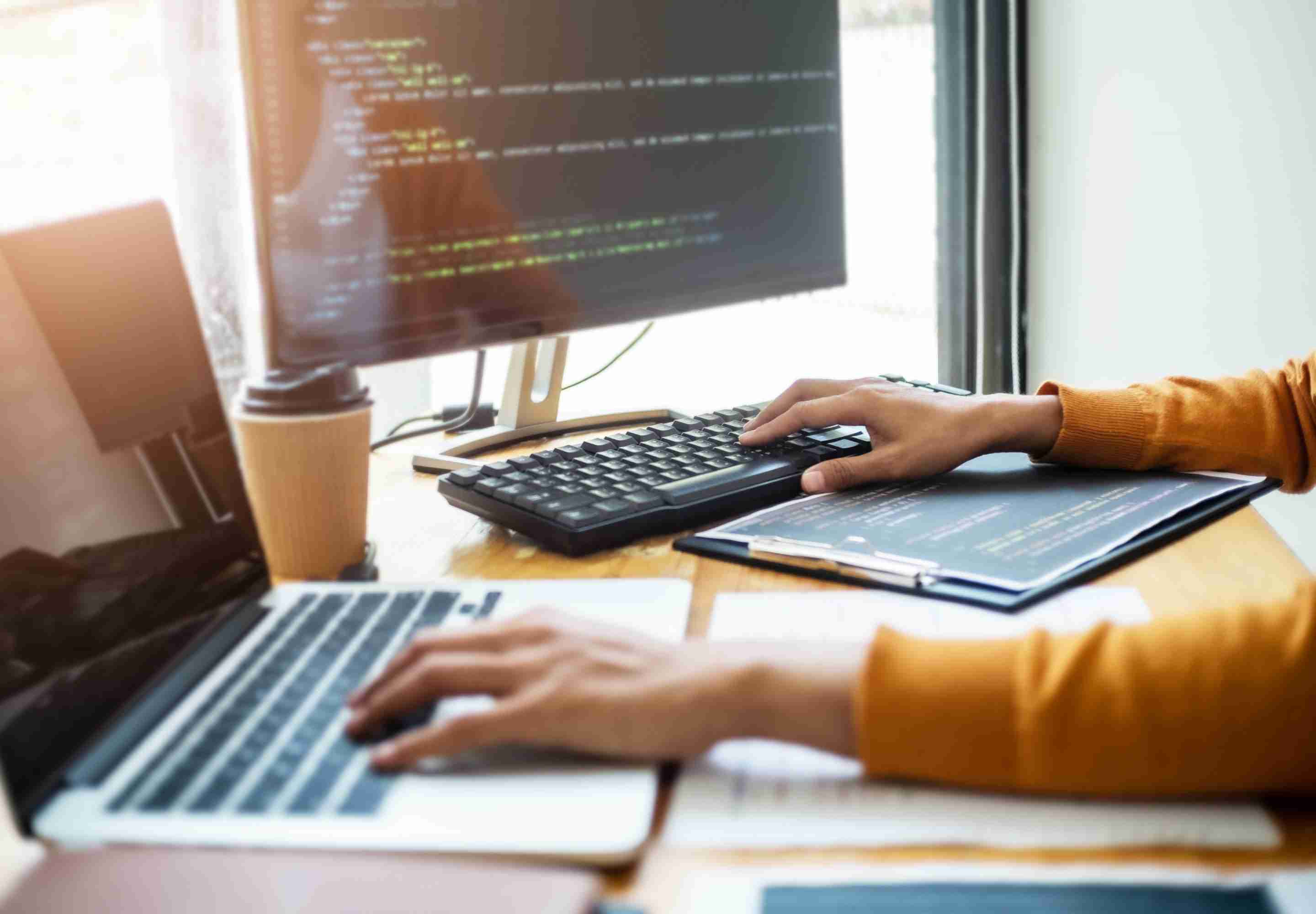Hands typing on laptop and desktop computer