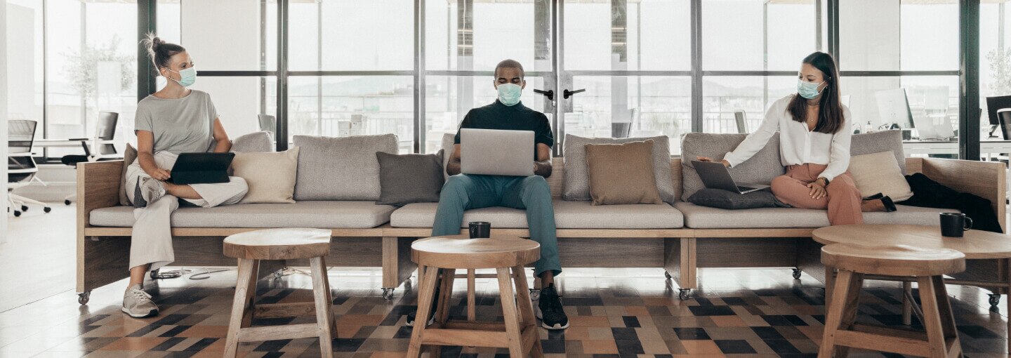 Three people working on laptops with masks