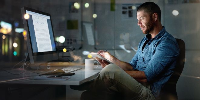 Man sitting in front of a laptop while looking at his mobile phone