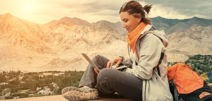 Woman sitting on an outside wall working on her laptop