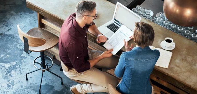 Man and woman sitting at a counter with a laptop and documents