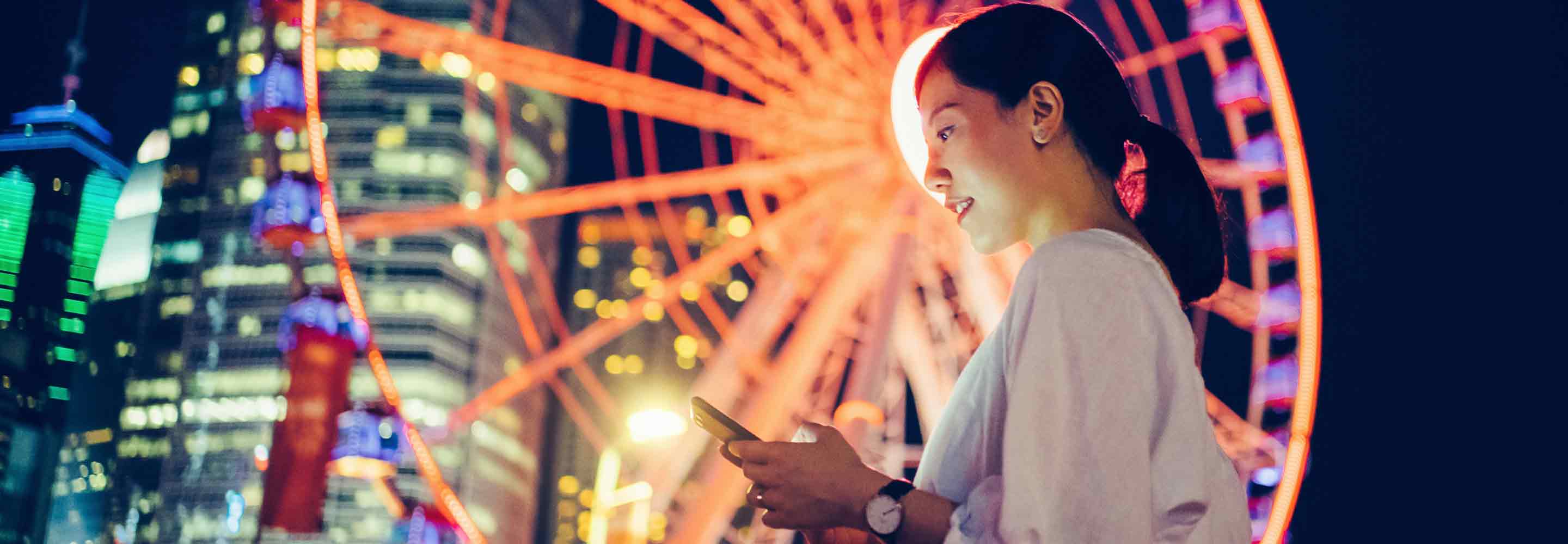 Smiling woman looking at her mobile phone at a ferris wheel