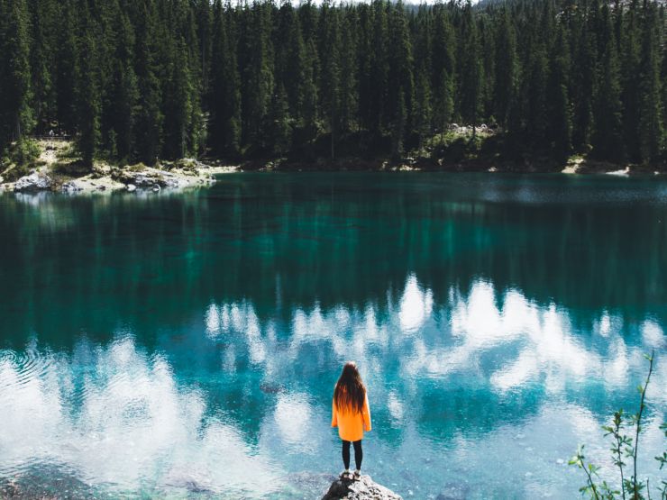 Woman at the edge of a lake looking at the mountain and trees reflecting 