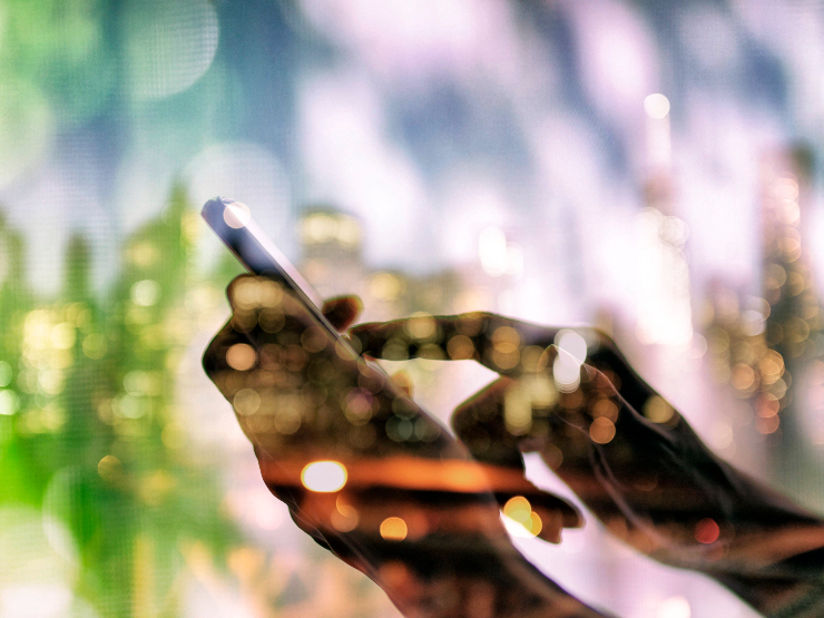 A silhouetted hand on their phone through a glass with reflections