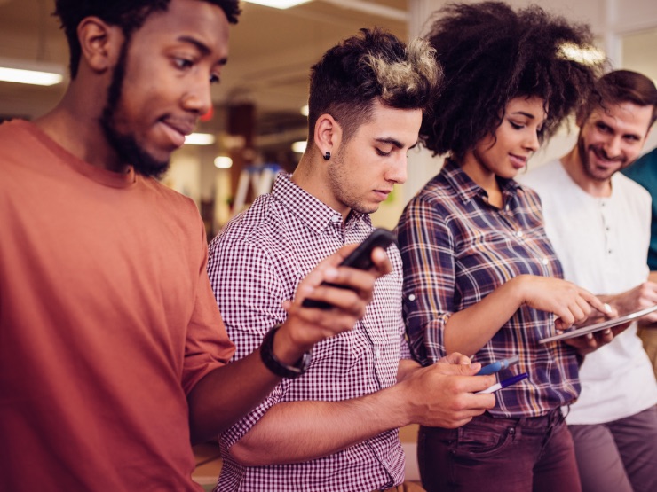 Four people standing in a row on their mobile devices