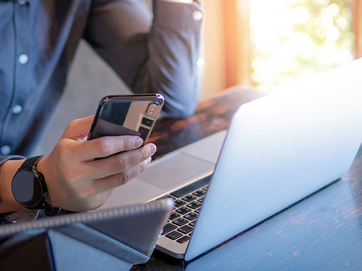 A guy holding a cellphone and has the laptop opened